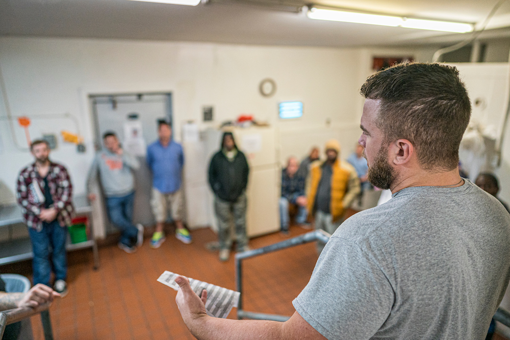 Jon Lewis standing in front of a group of guys speaking to them in a microphone