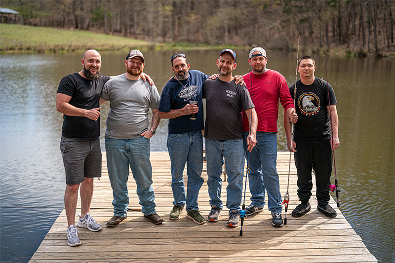 Group if men standing on the pier of a lake smiling at the camera