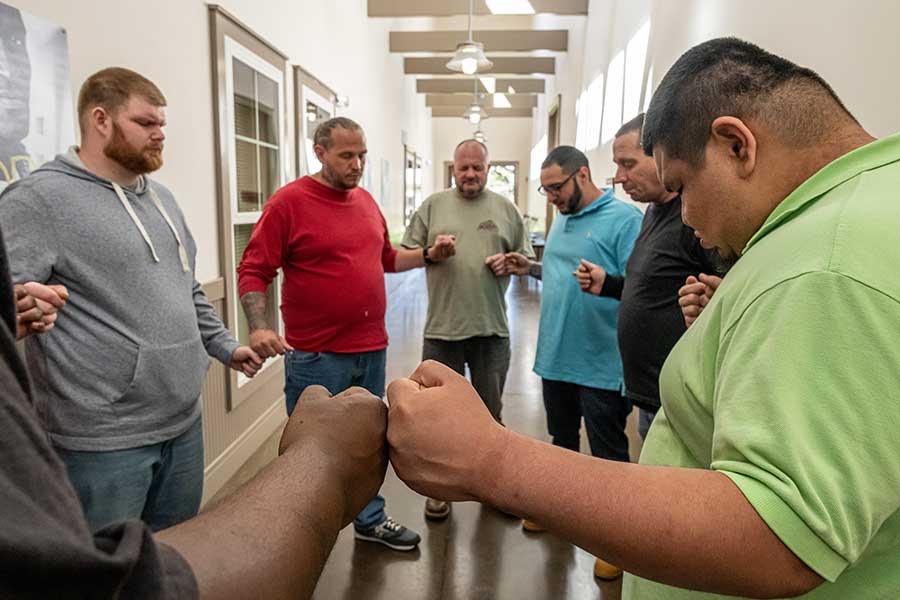 Photo of a group of men standing in a circle praying