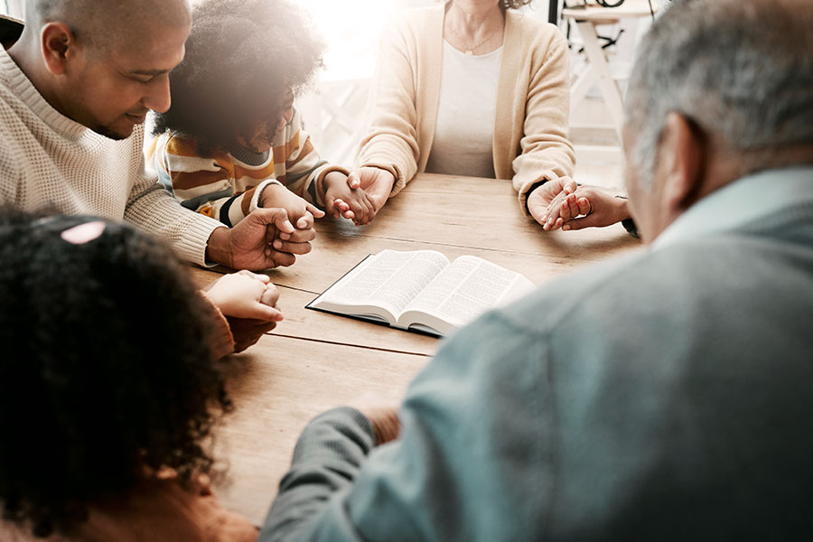 Photo of group of people sitting at a table holding hands in prayer