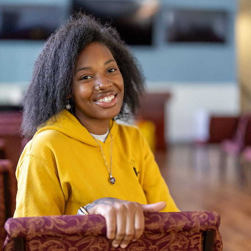 Woman wearing yellow hoodie and smiling at camera