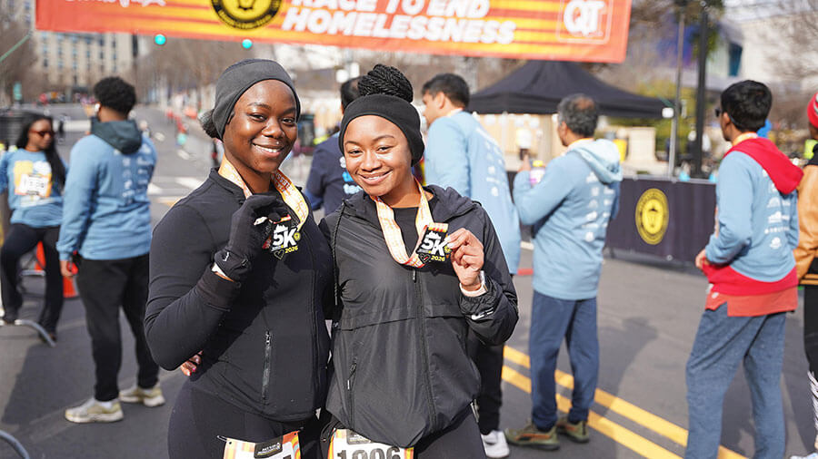 Two women posing at race finish line with their medals