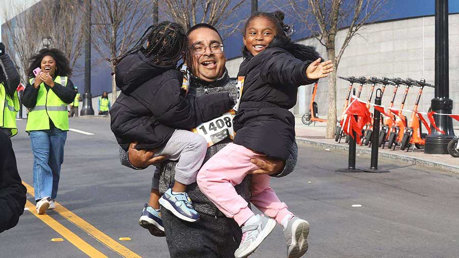A dad running the race holding two little girls in his arms