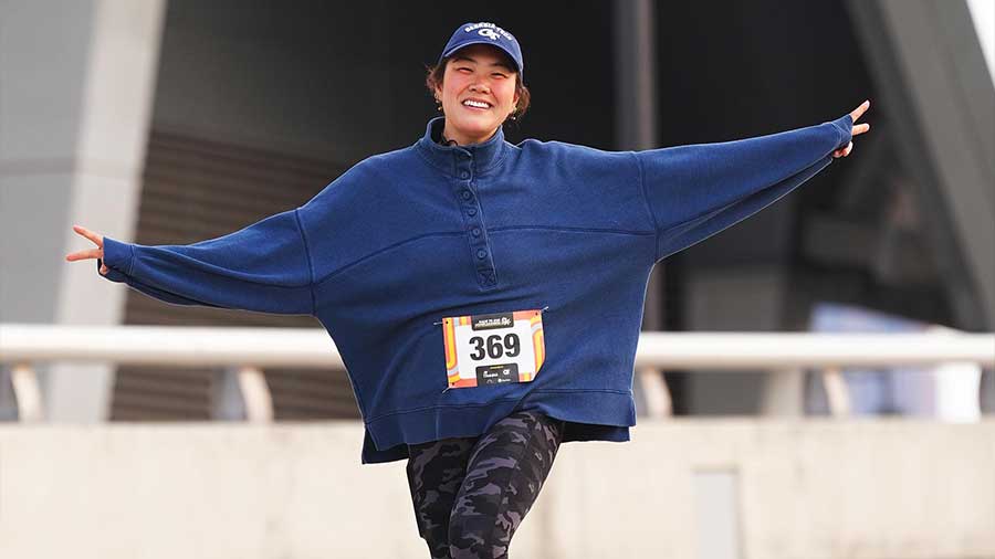 A woman running the race with arms outstretched smiling